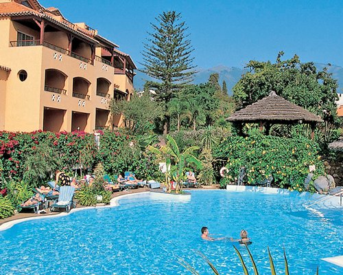 An outdoor swimming pool with patio furniture and sunshades alongside the resort.