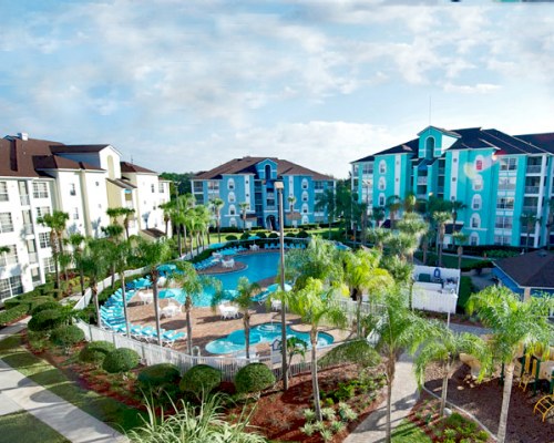 An outdoor swimming pool and chaise lounge chairs alongside multi story resort units.