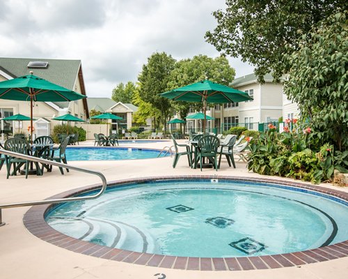 An indoor swimming pool with basketball setup chaise lounge chairs patio table sunshade and outside view.