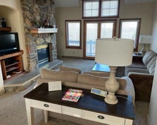 A well furnished living room with a television and stone fireplace.