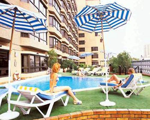 An outdoor swimming pool with sunshades and chaise lounge chairs alongside the resort.
