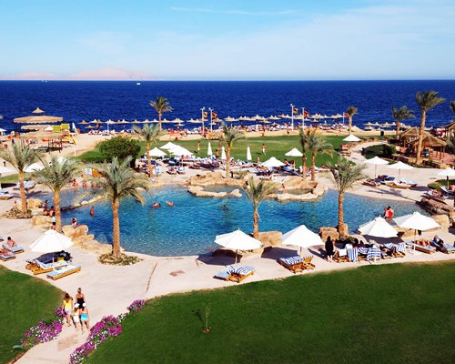 Scenic view of an outdoor swimming pool with chaise lounge chairs and sunshades alongside the beach.