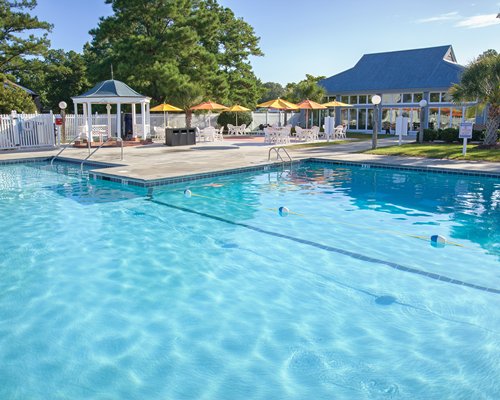 A scenic outdoor swimming pool with patio tables and sunshades alongside the resort.