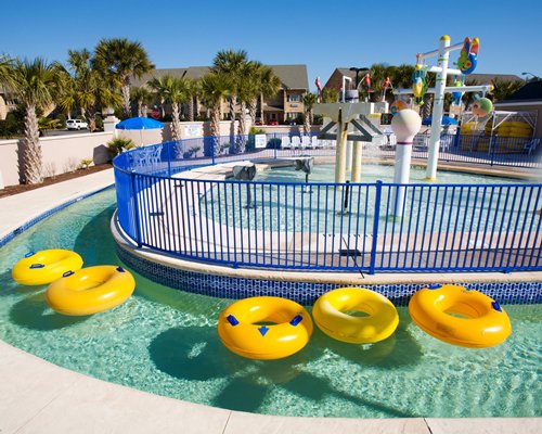 An outdoor water park with water sprinklers surrounded by palm trees.