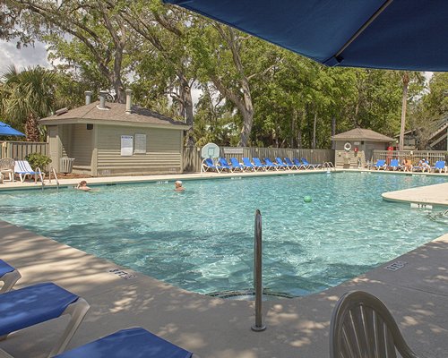 Outdoor swimming pool with chaise lounge chairs surrounded by wooded area.