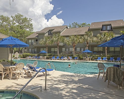 A view of outdoor swimming pool and hot tub with chaise lounge chairs and sunshades alongside the resort.