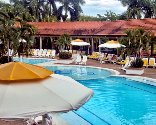 An outdoor swimming pool with sunshades and chaise lounge chairs alongside the resort.