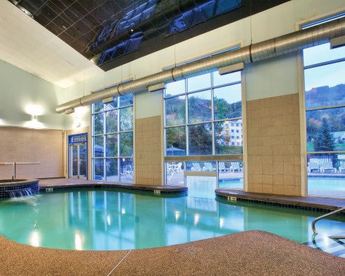 AN INDOOR SWIMMING POOL WITH A WATER FEATURE AND OUTSIDE VIEW.