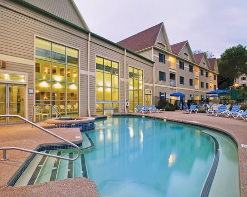 An outdoor swimming pool with a hot tub and chaise lounge chairs alongside multi story resort units.