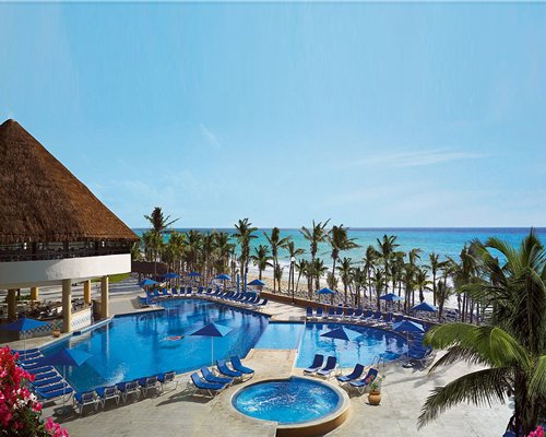 Outdoor swimming pool with a hot tub chaise lounge chairs sunshades and palm trees alongside the beach.