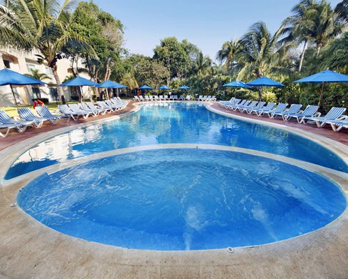 An outdoor swimming pool with a hot tub and chaise lounge chairs surrounded by trees.
