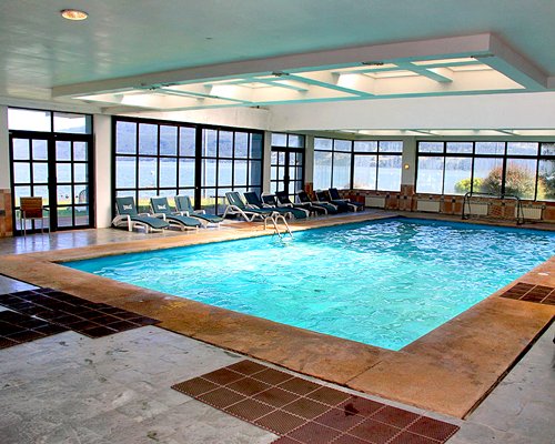Indoor swimming pool with chaise lounge chairs and outside view.
