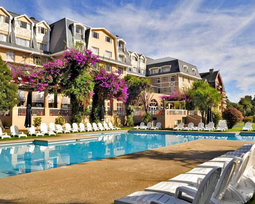 Scenic exterior view of Gran Hotel Pucon with an outdoor swimming pool and chaise lounge chairs.