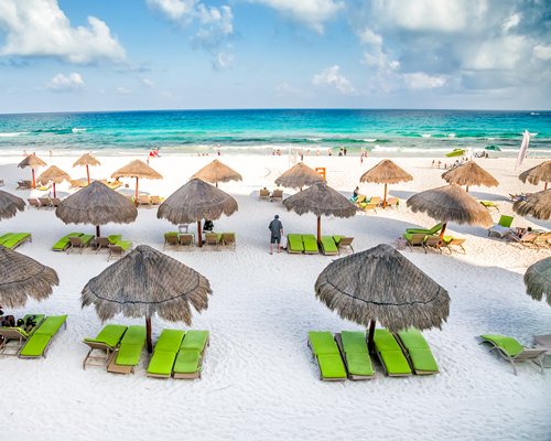A view of thatched sunshades with chaise lounge chairs alongside the beach.
