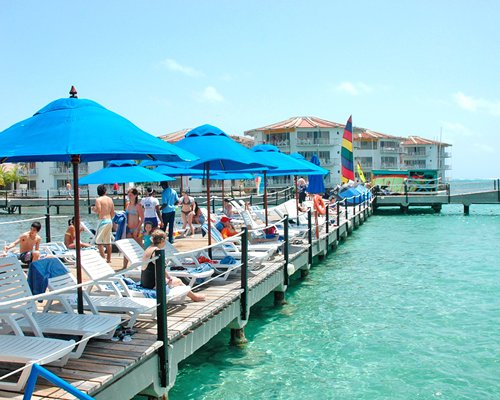 People on a wooden pier with chaise lounge chairs and sunshades alongside the sea.