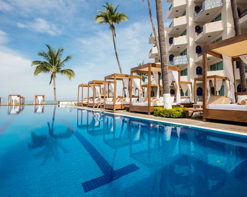 Large outdoor swimming pool with beach beds and palm trees alongside multiple unit balconies.