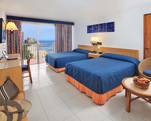 A well furnished bedroom with two beds television balcony and ocean view.