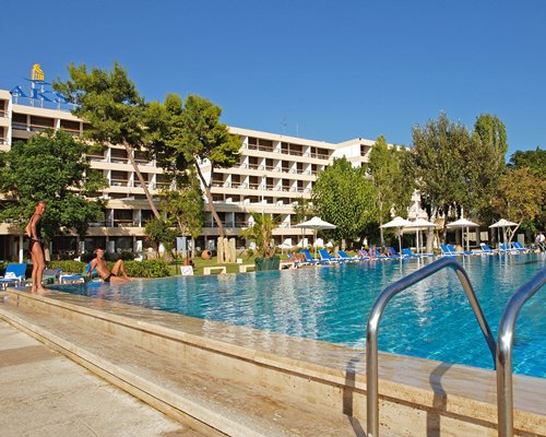 A large outdoor swimming pool with sunshades and chaise lounge chairs alongside the resort.