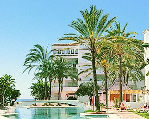 Exterior view of Heritage Resorts Club Playa Real with outdoor swimming pool pathway and palm trees.
