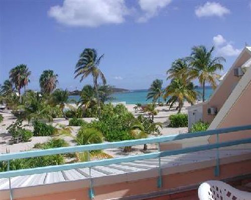 Balcony with patio chairs and view of the ocean with palm trees.