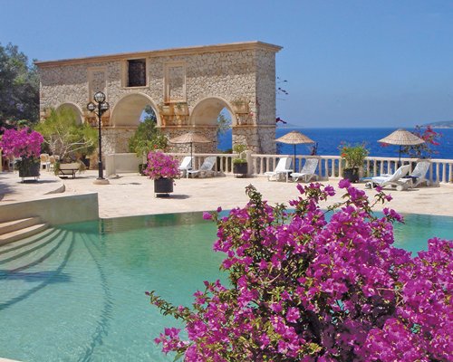 Scenic outdoor swimming pool with chaise lounge chairs and thatched sunshades alongside the sea.