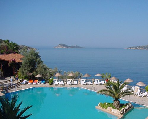 Outdoor swimming pool with chaise lounge chairs and sunshades alongside the ocean.