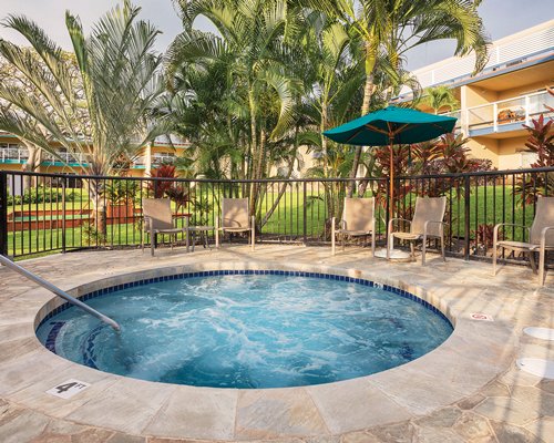 An outdoor hot tub with patio furniture and sunshades.