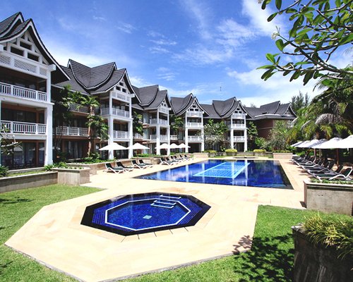 An outdoor swimming pool with a hot tub chaise lounge chairs and sunshades alongside multi story resort units.