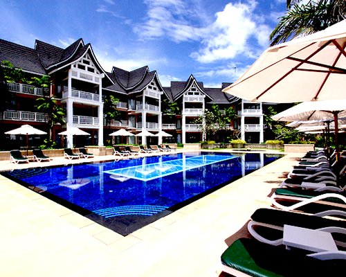 An outdoor swimming pool with chaise lounge chairs and sunshade alongside the multi story units.