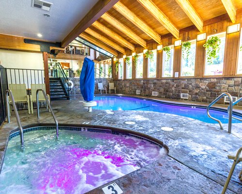 An indoor swimming pool with hot tub and patio alongside stairway.
