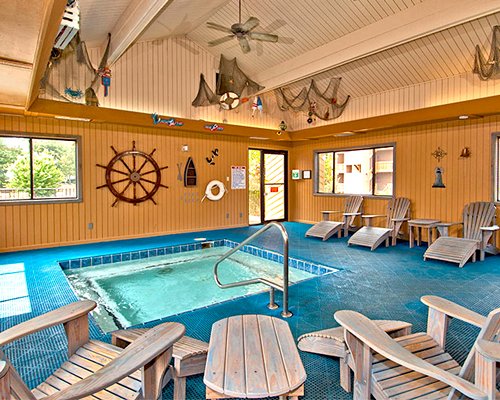 An indoor hot tub with chaise lounge chairs and an outside view.