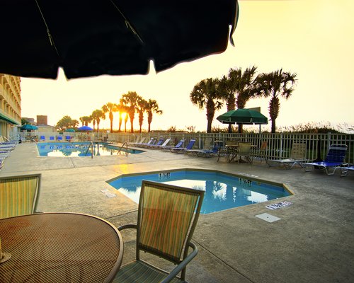 Outdoor swimming pool with hot tub dining chaise lounge chairs sunshades and palm trees.