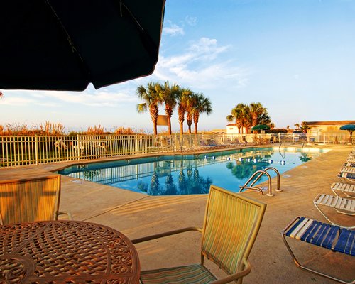 Outdoor swimming pool with chaise lounge chairs patio furniture and palm trees.