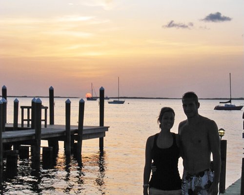 A couple at a wooden pier on the ocean with boats at dusk.