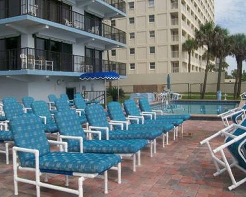 An outdoor swimming pool with sunshades and chaise lounge chairs alongside the resort.