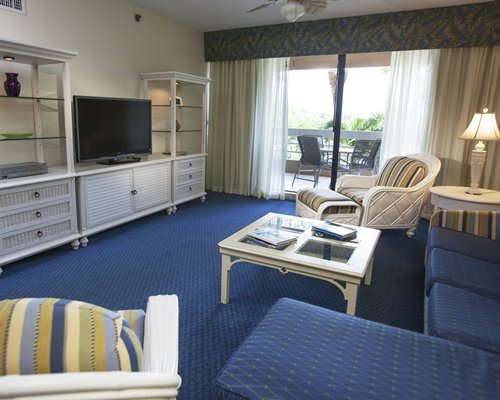 A well furnished living room with a television and balcony with patio chairs.