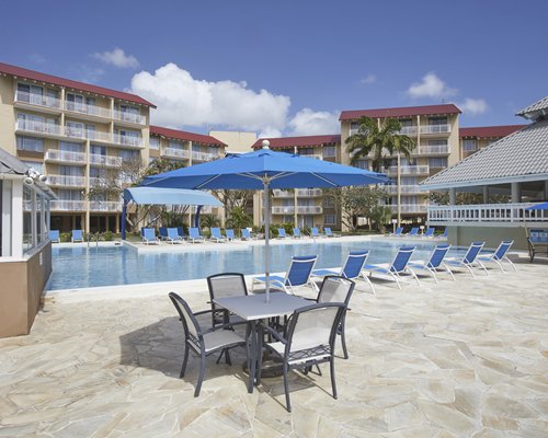 An outdoor swimming pool with a volleyball net and chaise lounge chairs alongside resort units.
