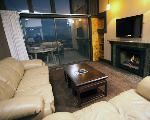 A well furnished living room with a television fire in the fireplace and an outside view.