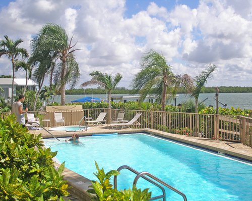 Outdoor swimming pool with a hot tub chaise lounge chairs and palm trees alongside the beach.