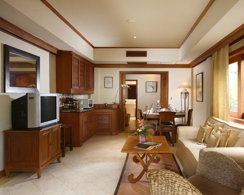 A well furnished living room with television open plan kitchen and dining area.