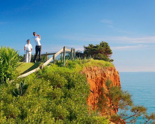 View of two man playing golf at the cliff edge at the resort alongside the ocean.