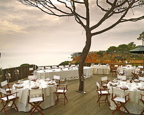 An outdoor fine dining area with a tree alongside the ocean.