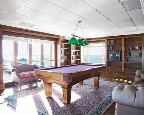 Indoor recreation room with pool table television bookshelf and bay view.