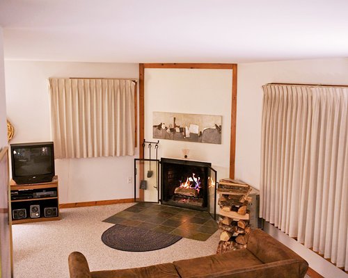 A well furnished living room with television and fire in the fireplace.