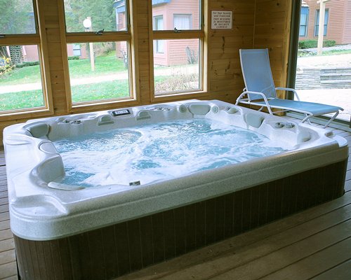 An indoor hot tub with chaise lounge chair and an outside view.