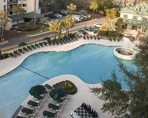 A large outdoor swimming pool with a fountain chaise lounge chairs and giant chess set alongside resort units.