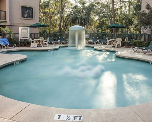 An outdoor swimming pool with raining mushroom umbrella alongside multi story resort units.