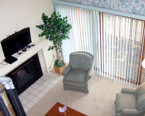 A well furnished living room with a fire in the fireplace television and outside view.