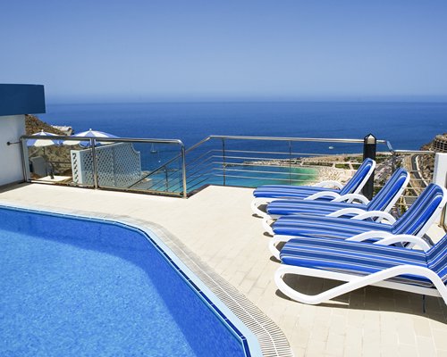 An outdoor swimming pool with chaise lounge chairs alongside the ocean.