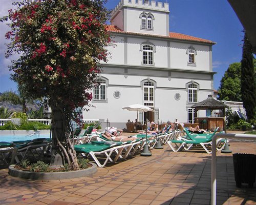 An exterior view of The Pestana Miramar resort with trees and chaise lounge chairs and sunshades.